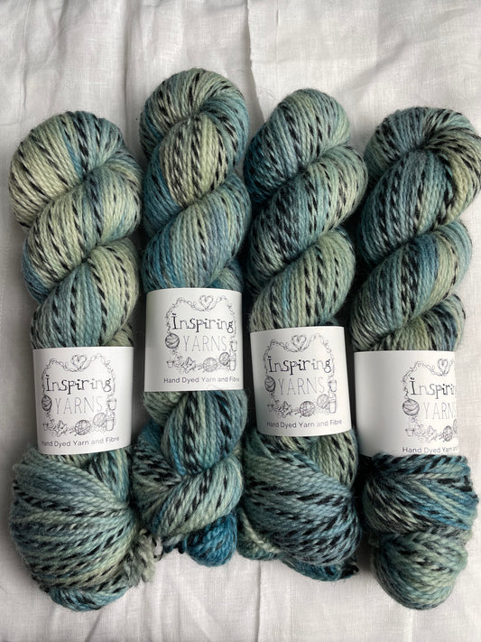 Four skeins of handyed Highland Zebra yarn in light green and teal blue colourway.  The yarn has black strands spun in to it. the skeins are labelled as Inspiring Yarns.