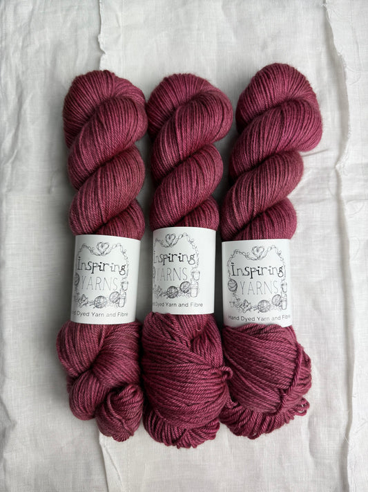 Three skeins of maroon yarn with labels on a textured white background