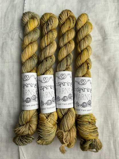 Four skeins of variegated yarn in soft cream and grey base with speckles in golden yellow, light aqua and earthy browns with Inspiring Yarns labels on a light textured background.