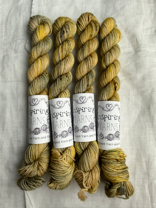 Four skeins of variegated yarn in soft cream and grey base with speckles in golden yellow, light aqua and earthy browns with Inspiring Yarns labels on a light textured background.