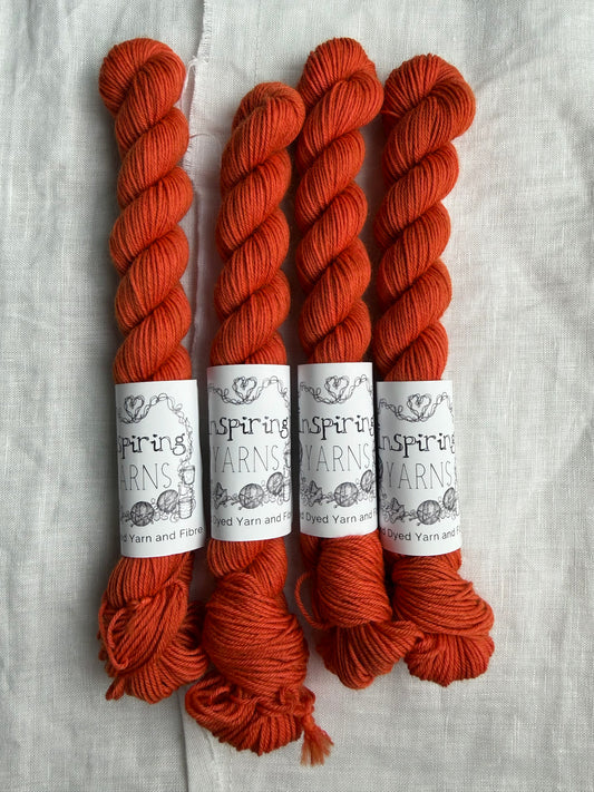 Four skeins of intense dark orange yarn with Inspiring Yarns labels on a light textured background.