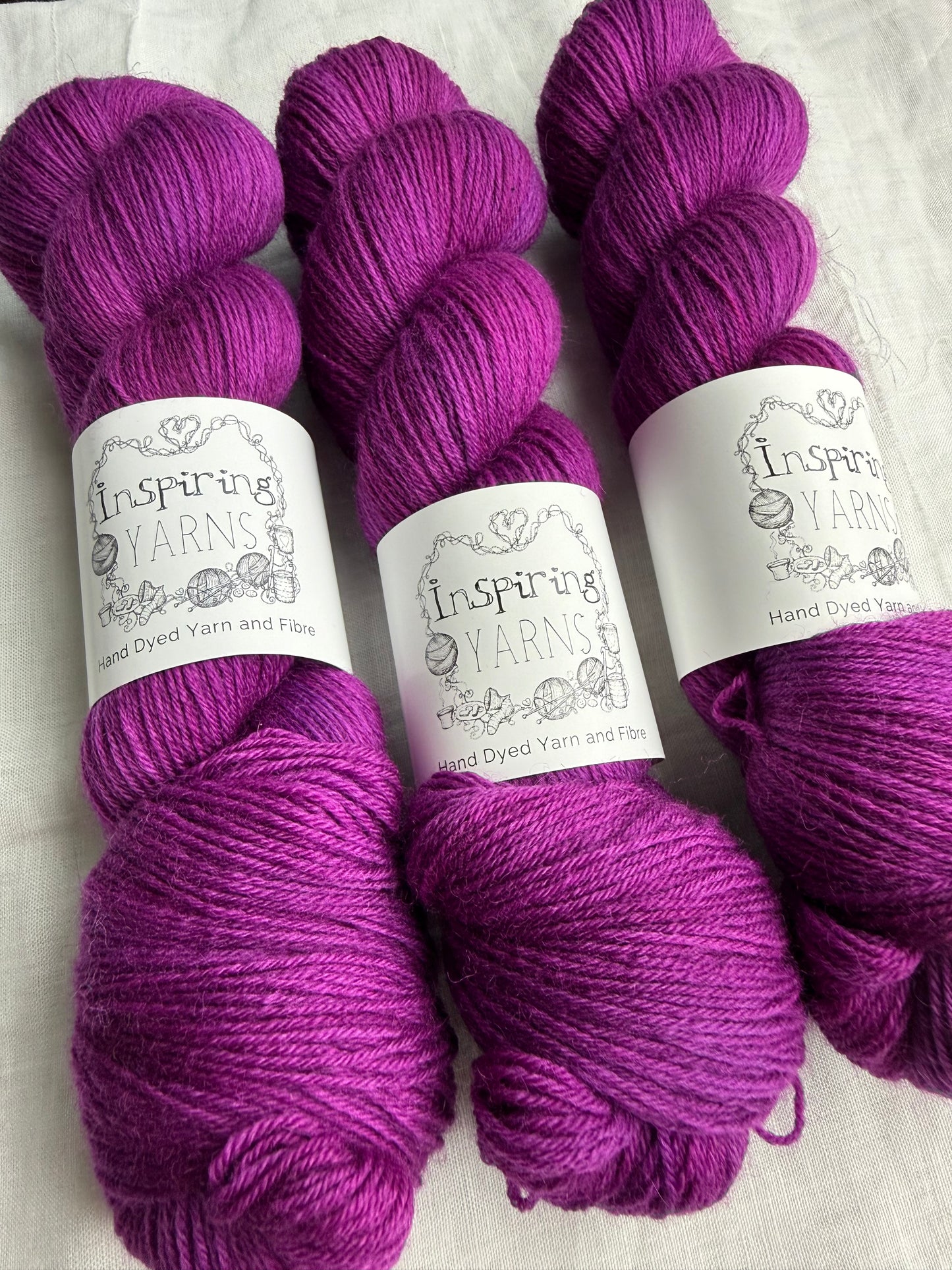 Three skeins of fuchsia tonal yarn labelled Inspiring Yarns on a white background