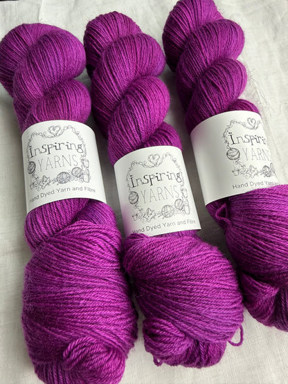 Three skeins of fuchsia tonal yarn labelled Inspiring Yarns on a white background