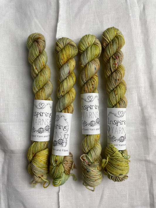 Four yellow based speckled mini skeins of Merino Smooth Sock yarn branded  Inspiring Yarns on a white linen fabric background. 