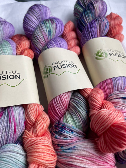 3 skeins of hand dyed yarn in a mix of purple, green and pink with vibrant blue and pink speckles, paired with a peach mini skein by Fruitful Fusion 