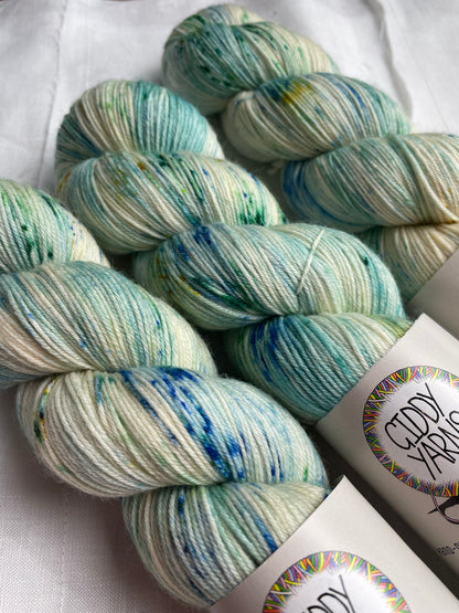 Close up of 3 skeins of of hand dyed yarn with blue and green speckles on a white background