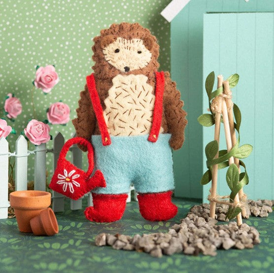 felt hedgehog with watering can, welly boots and shorts in a garden setting