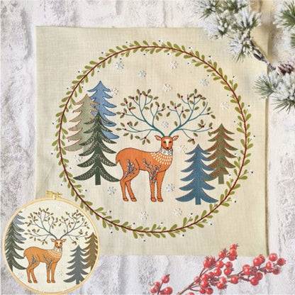 Embroidery featuring a decorative design with a deer surrounded by trees and foliage on a printed linen background.  Inset of the same design displayed in a wooden embroidery hoop.