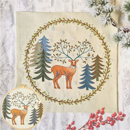 Embroidery featuring a decorative design with a deer surrounded by trees and foliage on a printed linen background.  Inset of the same design displayed in a wooden embroidery hoop.