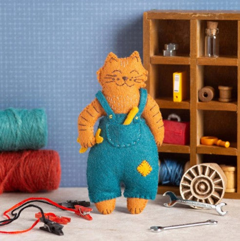 felt cat in mechanics overalls with mechanic set dressing in the background.