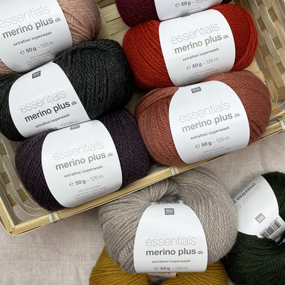 Assorted coloured skeins of yarn with 'essentials merino plus dk' labels in a woven basket.