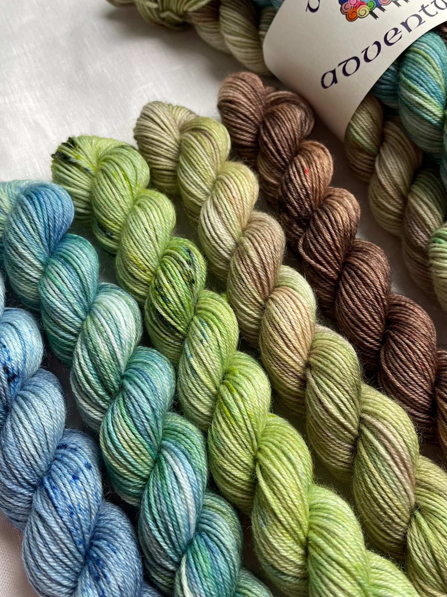 Close up of 2 sets of mini skeins in blue green brown fade on a white background