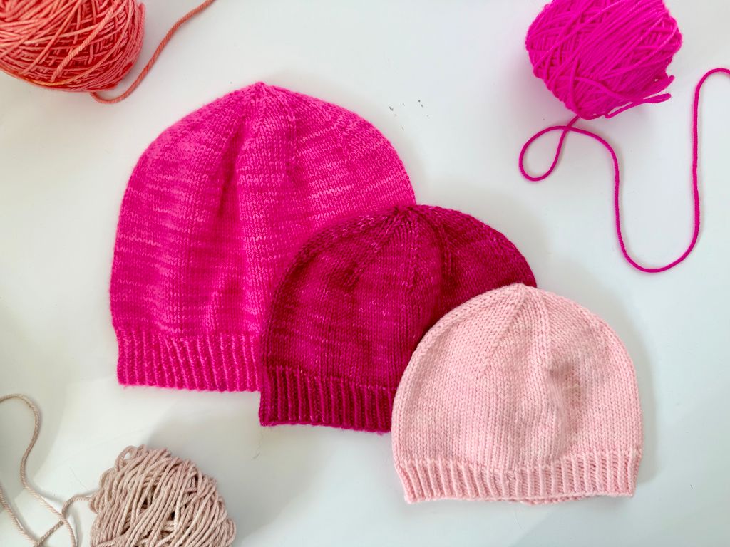 Three pink knitted hats with yarn balls on a light background.