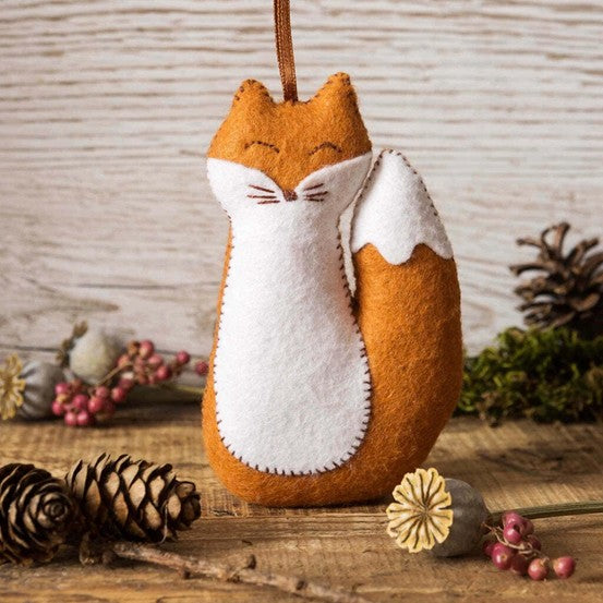 Felt fox ornament on a wooden surface with pine cones and berries