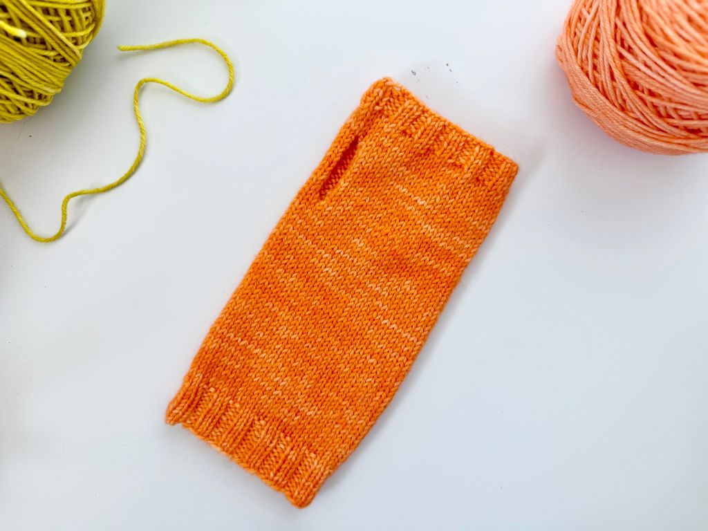 orange fingerless mitt with green and orange balls of yarn on white surface    