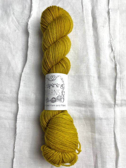 A skein of tonal ochre yellow coloured Highland 4Ply yarn branded Inspiring Yarns on a white linen background.