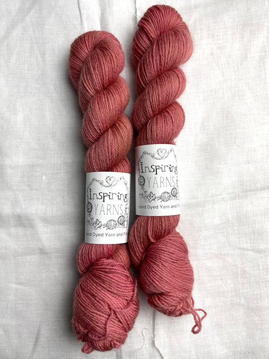 Two skeins of tonal dusky pink coloured Highland 4Ply yarn branded Inspiring Yarns on a white linen background.