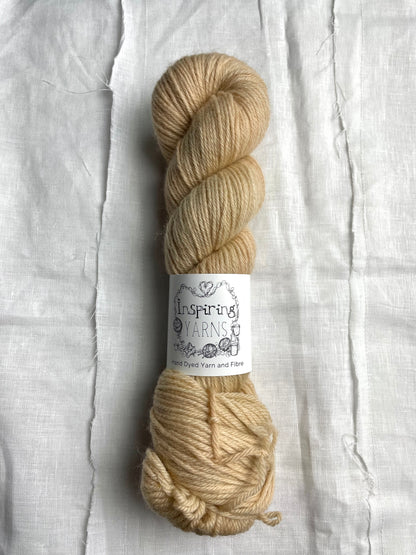 One skein of soft golden cream coloured Highland DK yarn branded Inspiring Yarns on a white linen background.