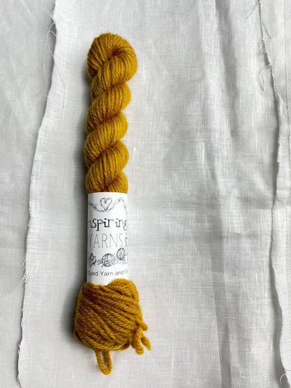 One skein of a tonal mustard coloured mini skein of Highland DK lies on a white linen background.