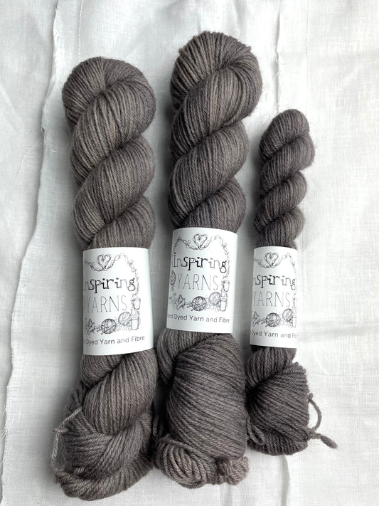 Skeins of tonal dark grey coloured Highland 4Ply yarn branded Inspiring Yarns on a white linen background.