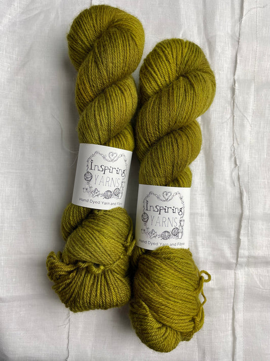 Two skeins of dark olive green coloured Highland DK yarn branded Inspiring Yarns on a white linen background.