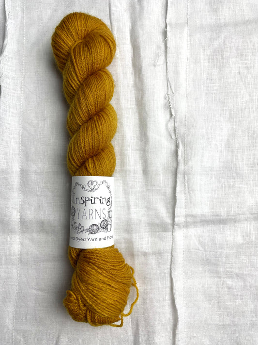 A skein of tonal mustard yellow coloured Highland 4Ply yarn branded Inspiring Yarns on a white linen background.