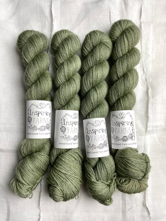 Skeins of tonal light green grey coloured Highland 4Ply yarn branded Inspiring Yarns on a white linen background.