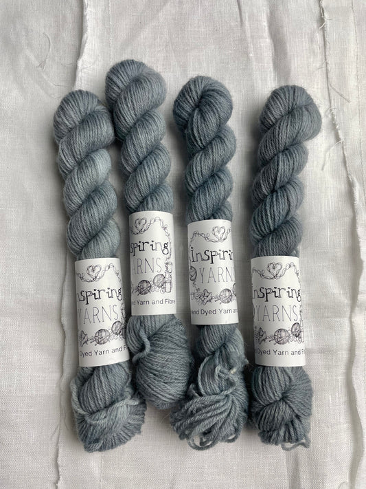 Skeins of tonal light grey blue coloured Highland 4Ply yarn branded Inspiring Yarns on a white linen background.