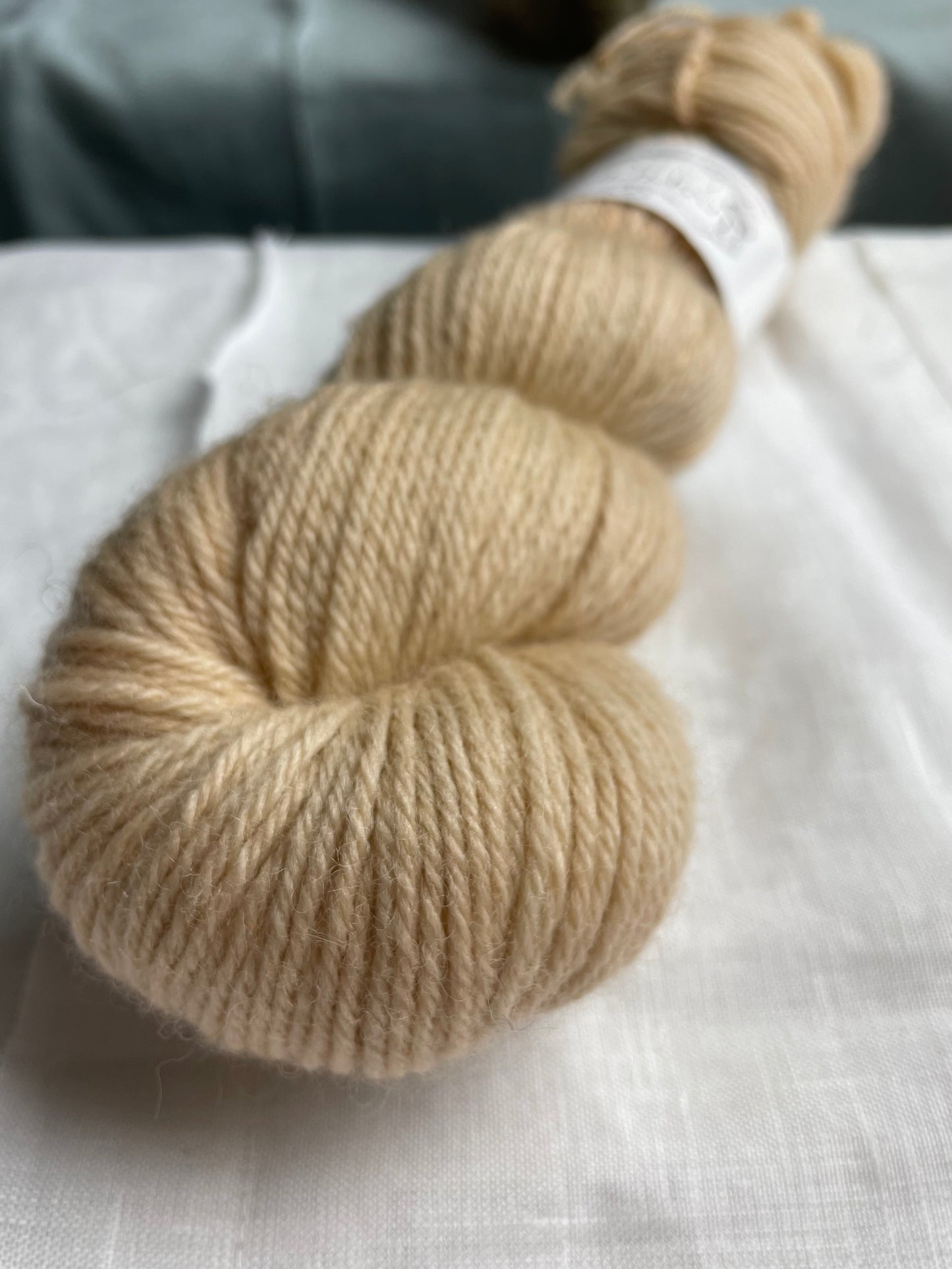 Close up of a skein of soft golden cream coloured Highland DK yarn branded Inspiring Yarns on a white linen background.