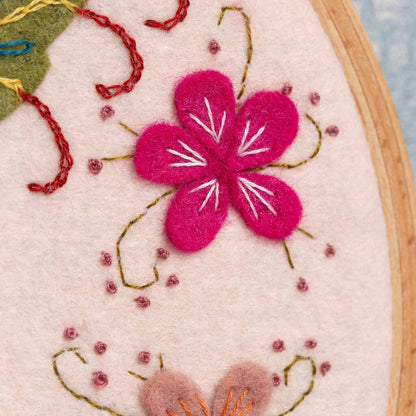 Close up of a embroidery hoop with pink flower and green leaves on a light background