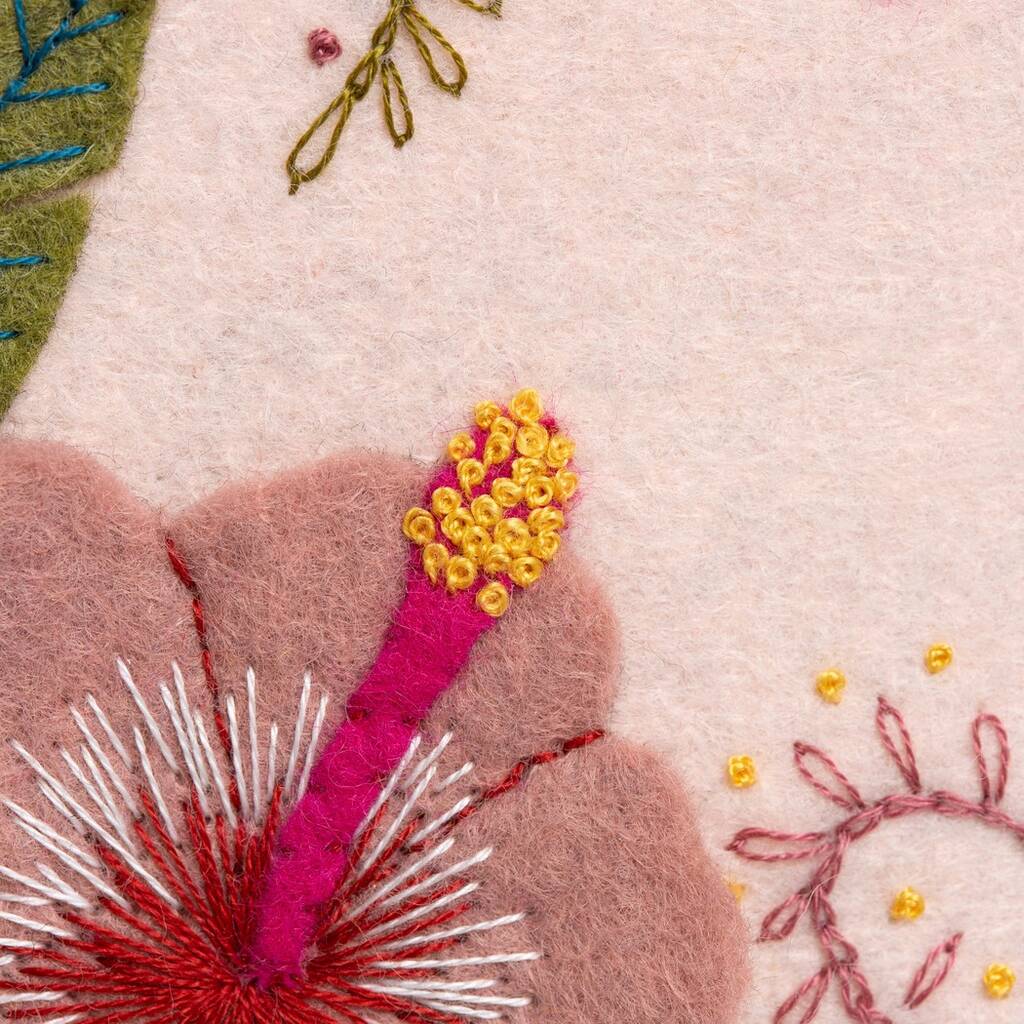 Close-up of embroidered floral design with pink, yellow, and green colors on a light pink background.