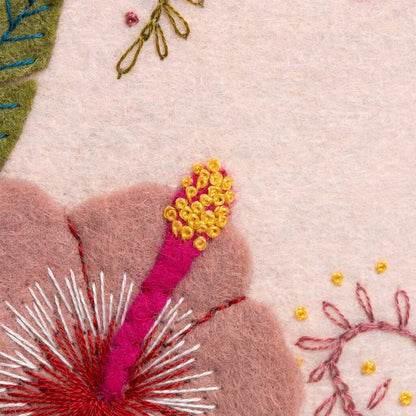 Close-up of embroidered floral design with pink, yellow, and green colors on a light pink background.