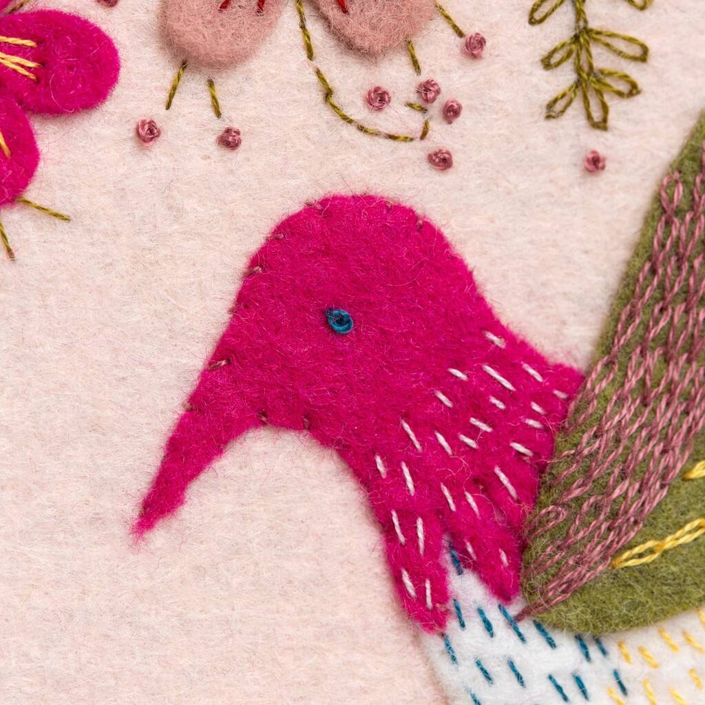 Embroidered pink bird with floral and leaf details on a light pink background