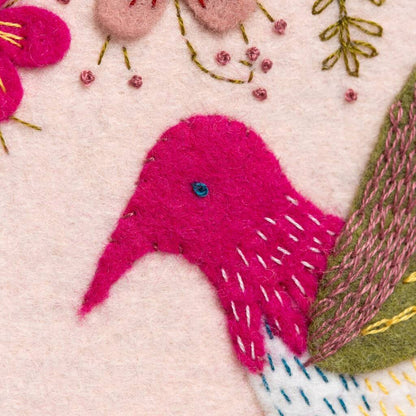 Embroidered pink bird with floral and leaf details on a light pink background