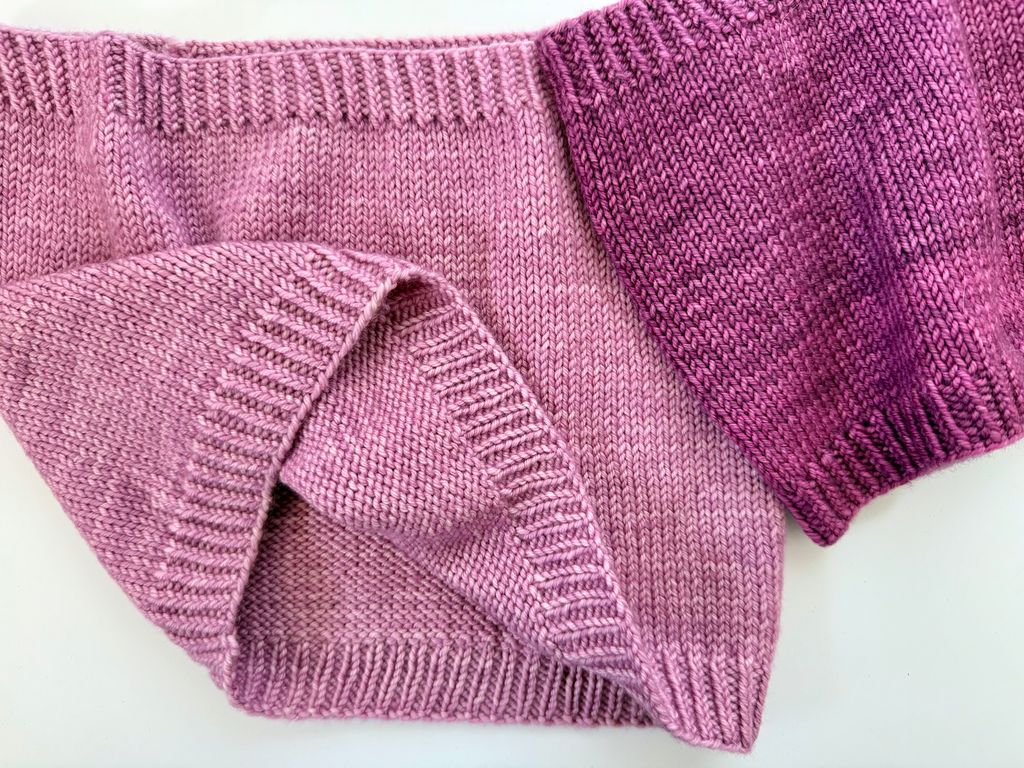 Close-up of a knitted fabric with a gradient from pink to purple on a white background. 
