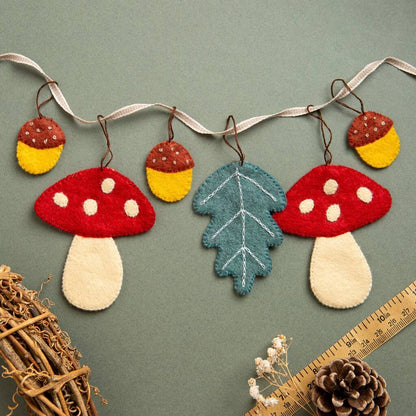 Decorative string with felt toadstools, acorns, and leaves on a green background. 
