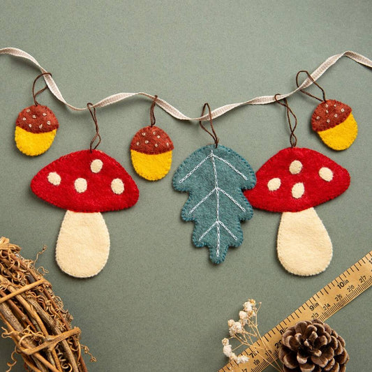 Decorative string with felt toadstools, acorns, and leaves on a green background. 